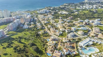 An aerial view of a coastal resort with multiple buildings, a swimming pool, and a view of the sea.