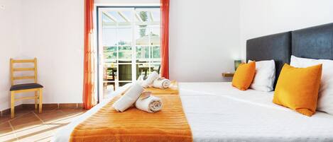 A hotel room with a bed, a chair, a table, and a view of the outdoors.
