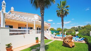 Une maison avec une piscine, des palmiers et un grand rocher dans le jardin.