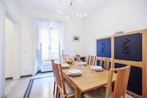 Un coin repas avec une table en bois dressée pour quatre personnes, des chaises, un lustre et une vue sur l’extérieur.