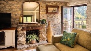 A stone fireplace with a TV, a sofa, and a large window overlooking a balcony. - Two-bedroom, pet friendly holiday cottage set in Fowey and within walking distance of the beach (Fowey)