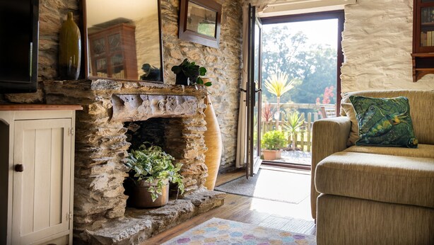 A stone fireplace with plants, a wooden cabinet, and a sofa with a cushion. - Two-bedroom, pet friendly holiday cottage set in Fowey and within walking distance of the beach (Fowey)