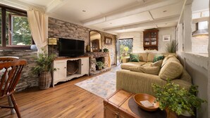 A cozy living room with a stone wall, wooden floor, a television, a fireplace, a sofa, and a dining area with a wooden table and chairs. - Two-bedroom, pet friendly holiday cottage set in Fowey and within walking distance of the beach (Fowey)