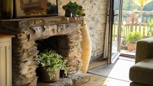 A stone fireplace with plants, a wooden cabinet, and a view of the outdoors. - Two-bedroom, pet friendly holiday cottage set in Fowey and within walking distance of the beach (Fowey)