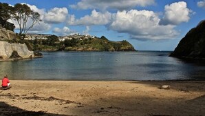 A beach with a clear view of the sea, a sandy shore, and a building with a red roof in the foreground. - Two-bedroom, pet friendly holiday cottage set in Fowey and within walking distance of the beach (Fowey)