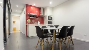 Una cucina moderna con piastrelle rosse, un piano di lavoro bianco e sedie nere attorno a un tavolo.