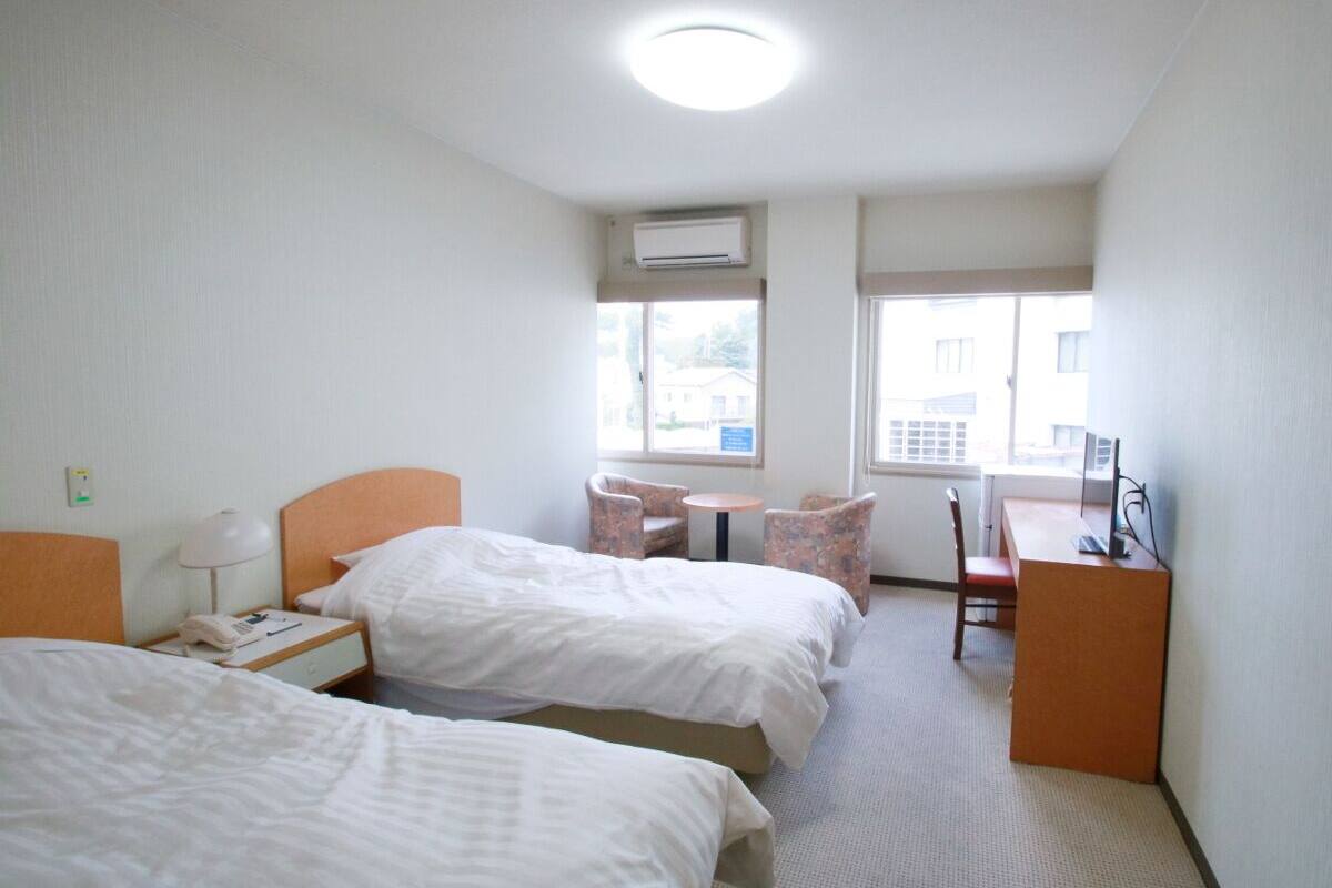 Ein Hotelzimmer mit zwei Betten, einem Schreibtisch, einem Stuhl, einem kleinen Tisch und einer Klimaanlage.