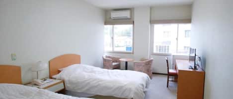 A hotel room with two beds, a desk, a chair, a small table, and a window.