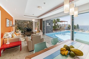 A modern living room with a stone wall, a pool, and a view of the ocean. - Character villa, access to beach| Villa Do Mar III (Arco Da Calheta)