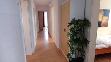 A hallway with wooden flooring, a potted plant, and a bed with a wooden frame.