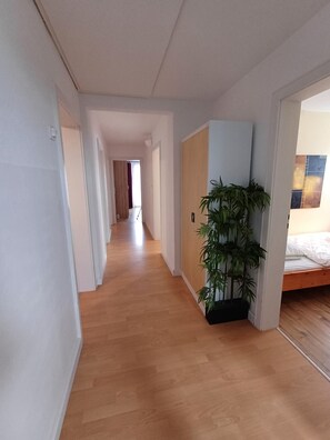 Un pasillo con suelo de madera, una planta en maceta y una cama con estructura de madera.