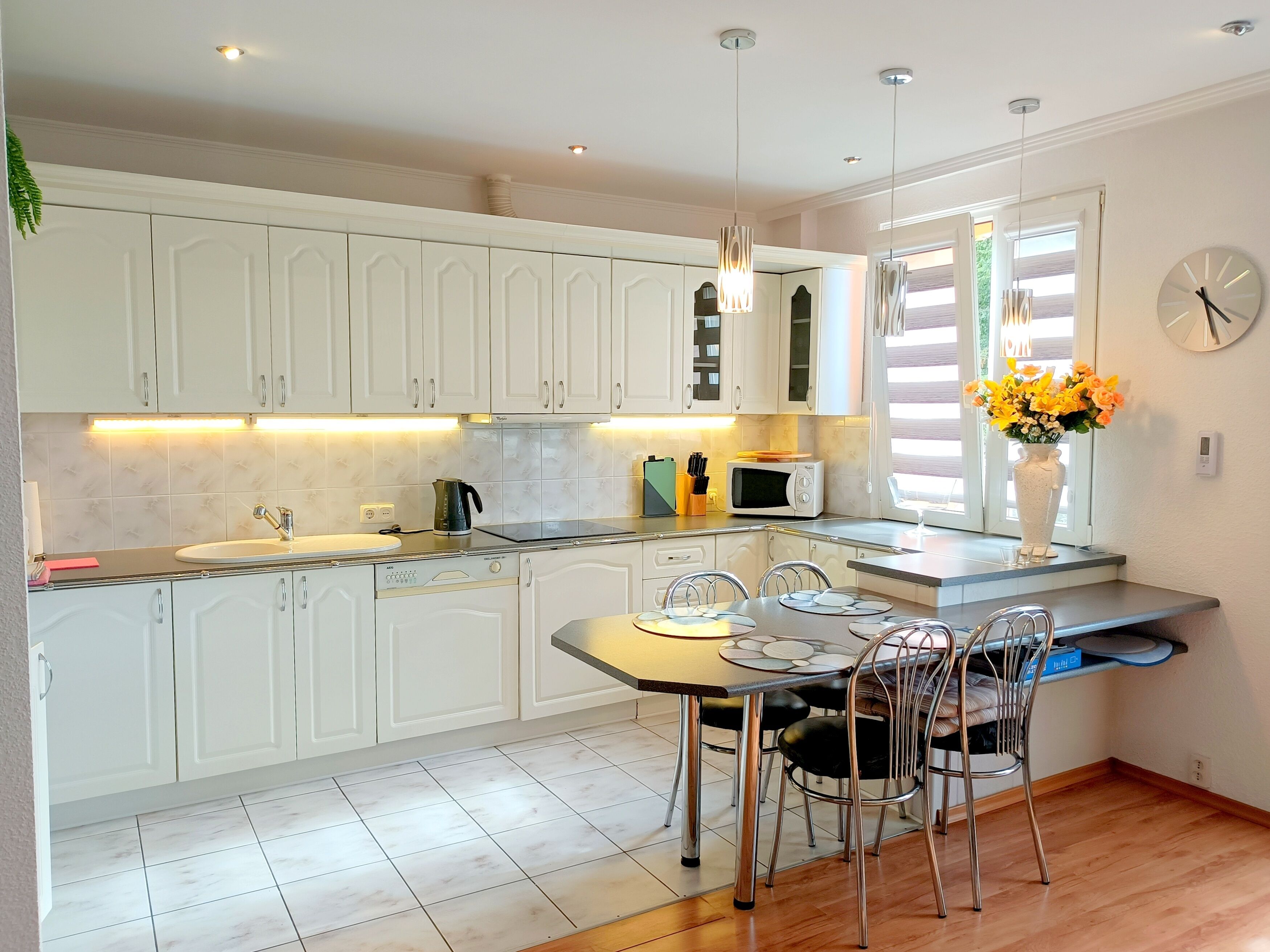 A modern kitchen with white cabinets, a dining table with chairs, a microwave, and a vase with flowers.