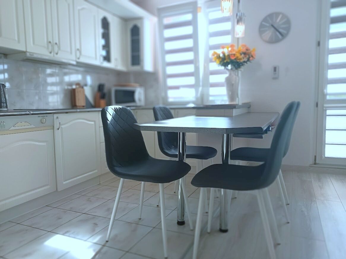 Una cocina moderna con armarios blancos, una mesa de comedor con cuatro sillas y un reloj en la pared.