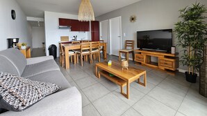 Een moderne woonkamer met een grijze bank, een houten eettafel en een televisie op een houten dressoir.