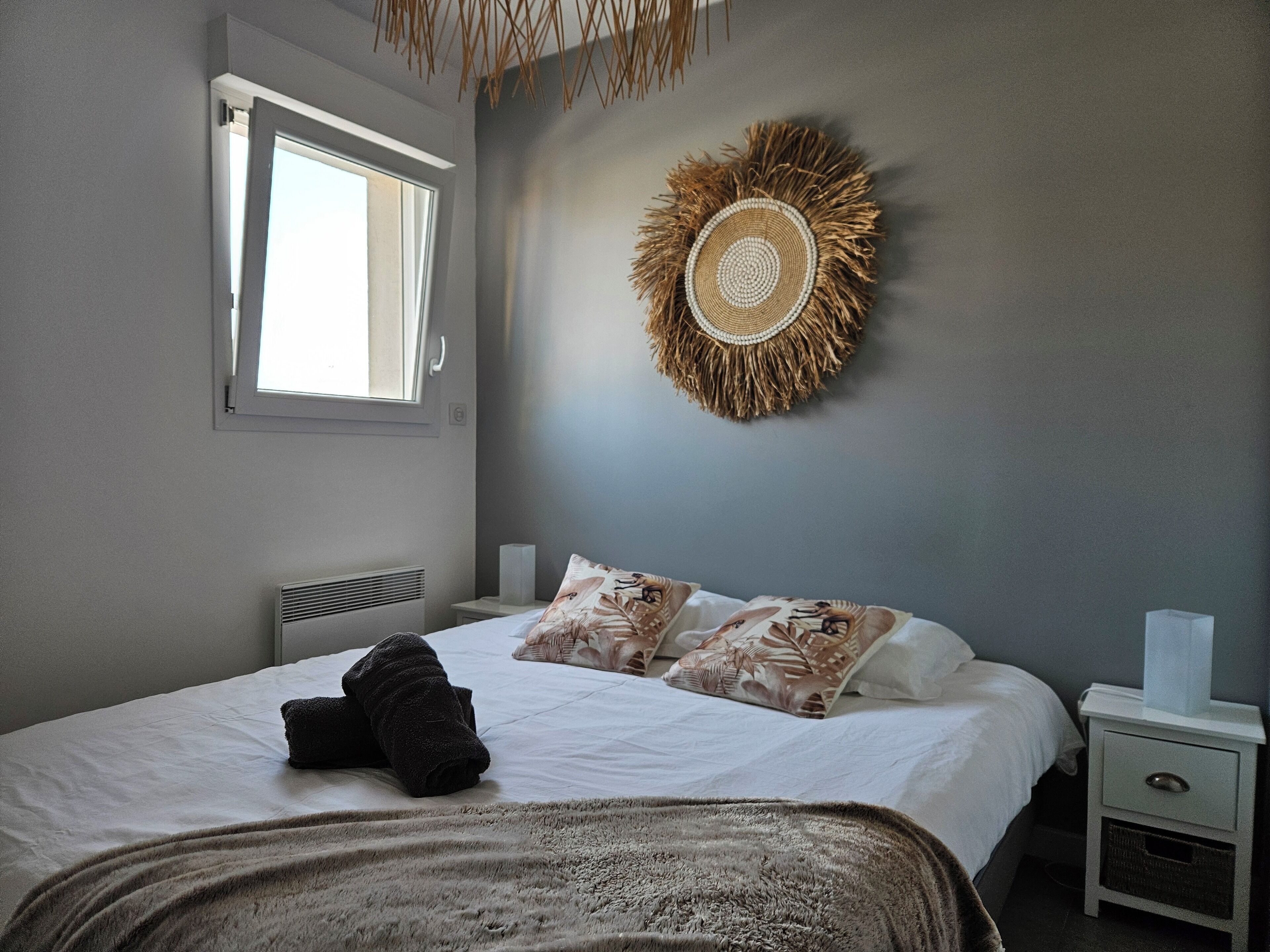 Ein Schlafzimmer mit einem Bett, einem Nachttisch, einer Wanddekoration und einem Fenster.