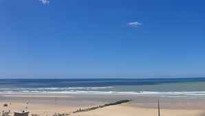 Een strand met heldere lucht, rustige zee en een zandstrand met een wachthuisje.
