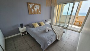 Een slaapkamer met een groot bed, een wereldkaart aan de muur, een nachtkastje en uitzicht op zee door een schuifdeur.
