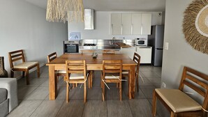 A modern kitchen with white cabinets, a wooden dining table, and a hanging light fixture. - Pasino bright apartment,+Terrace15m²,face mer, WIFI, Parking included, 8p,N°6 (Lacanau)