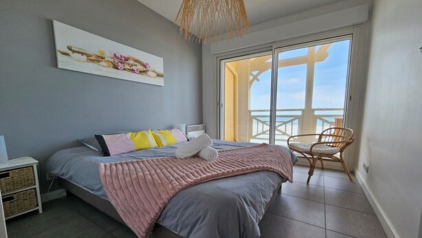 A bedroom with a bed, a chair, a painting, and a view of the beach through a large window. - Pasino bright apartment,+Terrace15m²,face mer, WIFI, Parking included, 8p,N°6 (Lacanau)