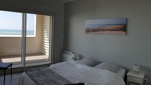 Ein Schlafzimmer mit einem großen Bett, Meerblick durch eine Schiebetür, einem Nachttisch mit Lampe und einem Wandbild.