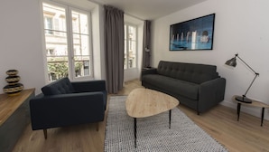 Een moderne woonkamer met een grijze bank, een zwarte fauteuil, een houten salontafel en een kamerkleed met een patroon.