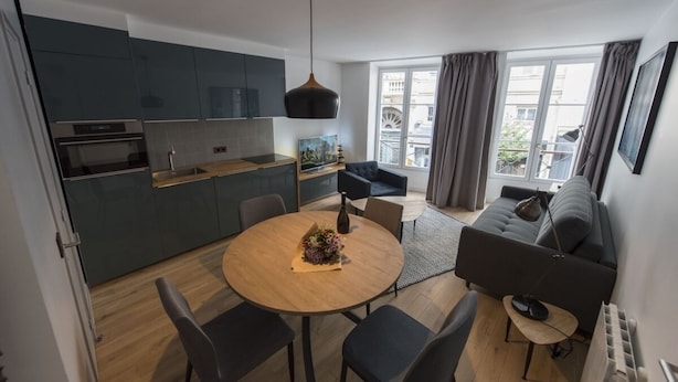 Een moderne keuken met donkere kasten, een eettafel met stoelen en een bank in een woonruimte met uitzicht op de stad.
