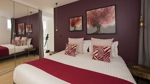 Een moderne slaapkamer met een groot bed, twee aan de muur bevestigde schilderijen, een spiegel en een nachtkastje.