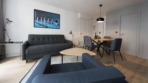 Een moderne woonkamer met een grijze bank, een ronde salontafel en een eethoek met een tafel en stoelen.