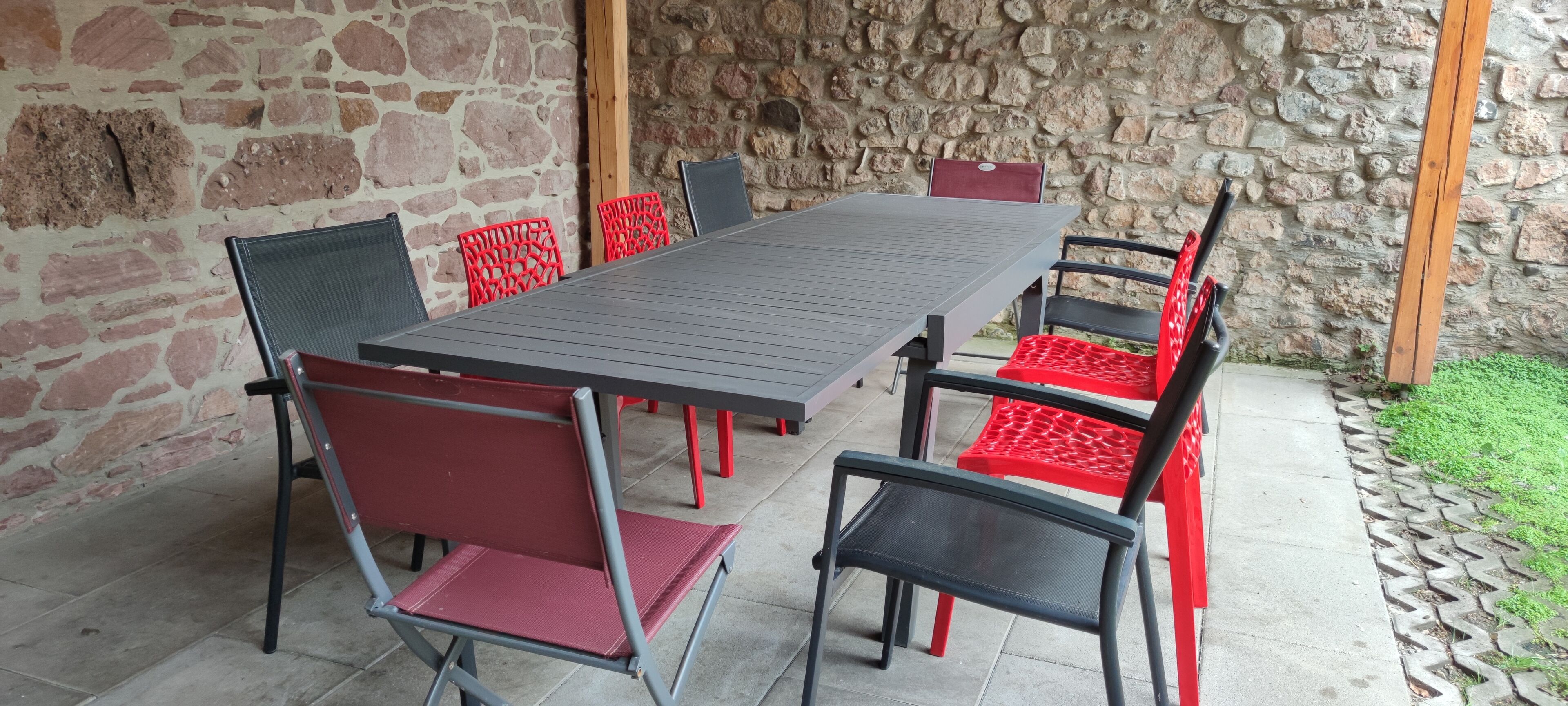 Une terrasse extérieure avec une table rectangulaire et six chaises, dont certaines sont dotées de coussins rouges.