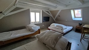 Ein Schlafsaalzimmer mit zwei Einzelbetten, einem an der Wand montierten Fernseher, einem Fenster und einem kleinen Tisch.