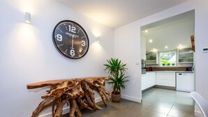 A modern kitchen with white cabinets, a wooden dining table, a large clock, and a potted plant.