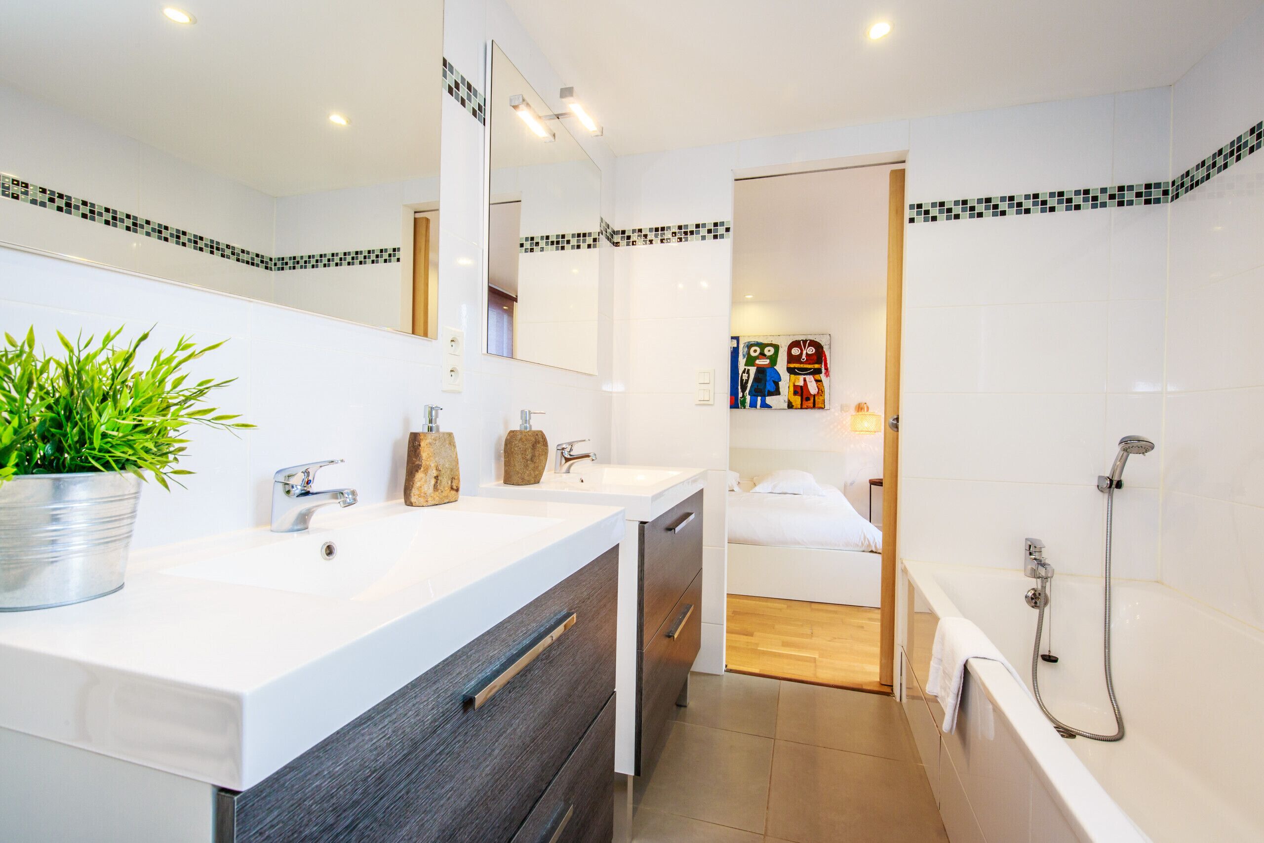 Een moderne badkamer met een wit wastafelmeubel, een spiegel, een douche en een plant in pot.