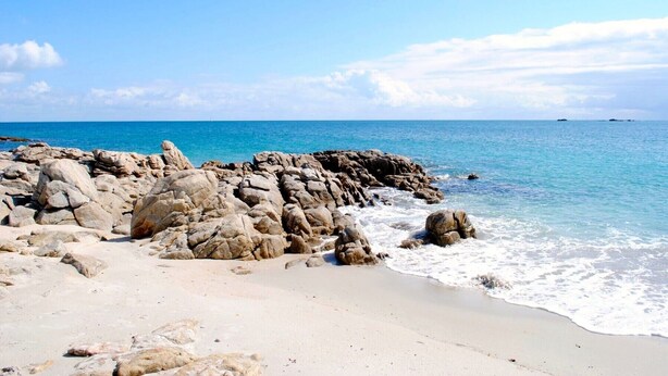 A rocky beach with clear blue water and a sandy shore.