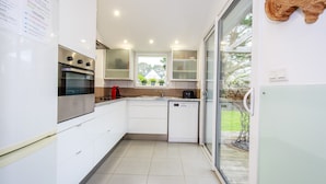 A modern kitchen with white cabinets, a built-in oven, a dishwasher, and a window overlooking a garden.