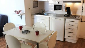 A modern kitchen with white cabinets, a microwave, and a coffee machine. There is a dining table with chairs and a small decorative item on the wall.