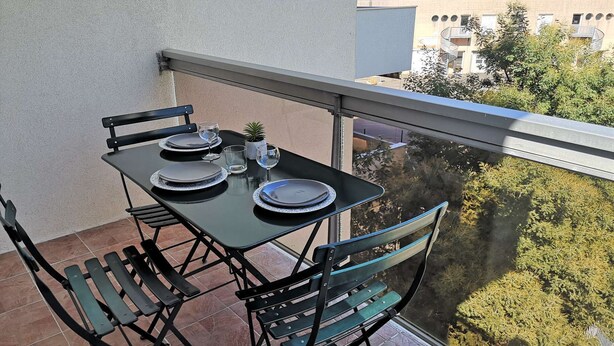 A balcony with a table set for two, chairs, and a potted plant.