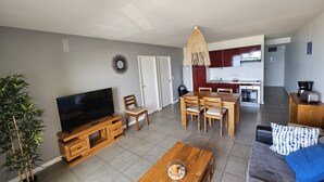A modern living room with a flat-screen TV, wooden furniture, a dining area, and a kitchen in the background. - Pasino bright apartment +Terrace15m2, seafront, WIFI, Parking included, 6p,N°5 (Lacanau Océan)