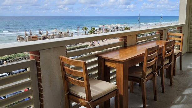 A balcony with a wooden table and chairs, overlooking a beach with people and umbrellas. - Pasino bright apartment +Terrace15m2, seafront, WIFI, Parking included, 6p,N°5 (Lacanau Océan)
