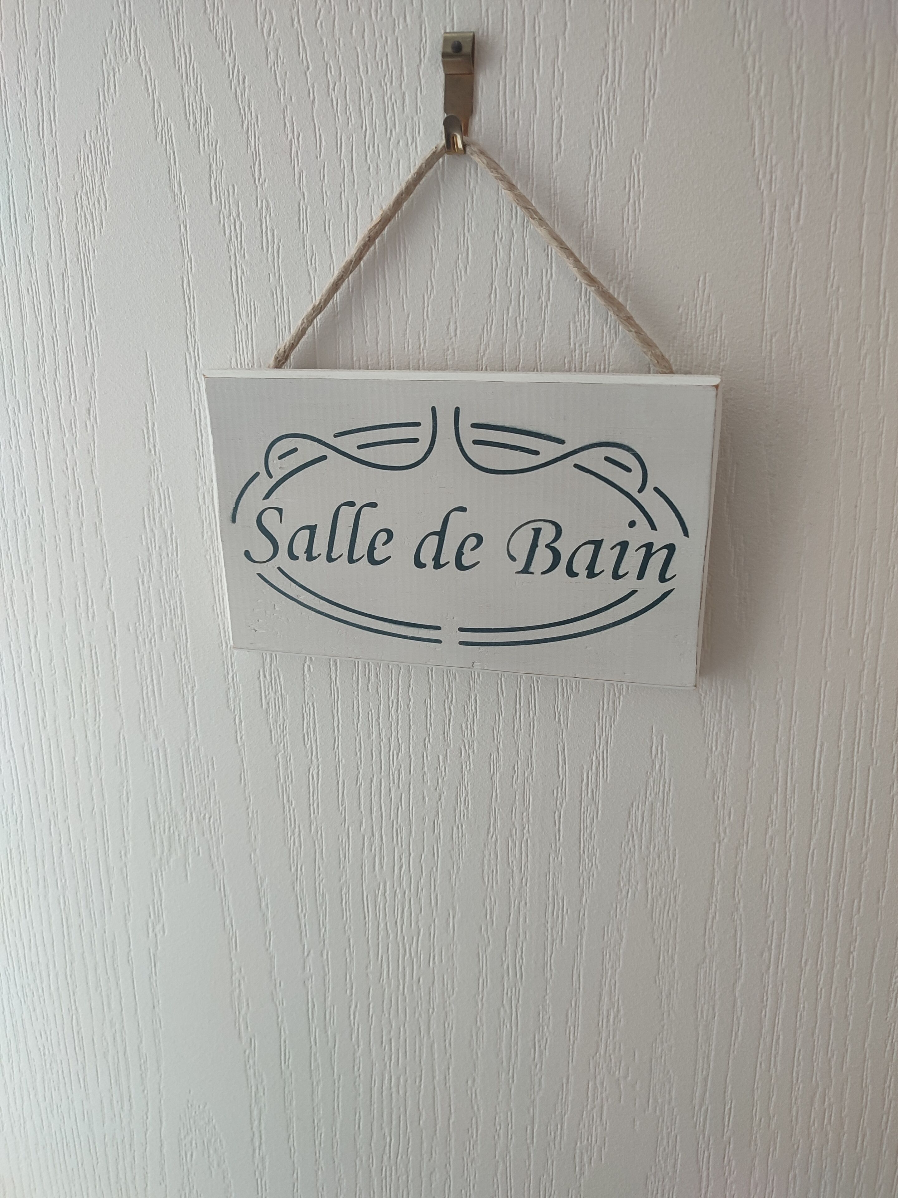 A sign with the text "Salle de Bain" hanging on a textured wall.