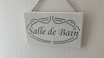 A sign with the text "Salle de Bain" hanging on a textured wall.