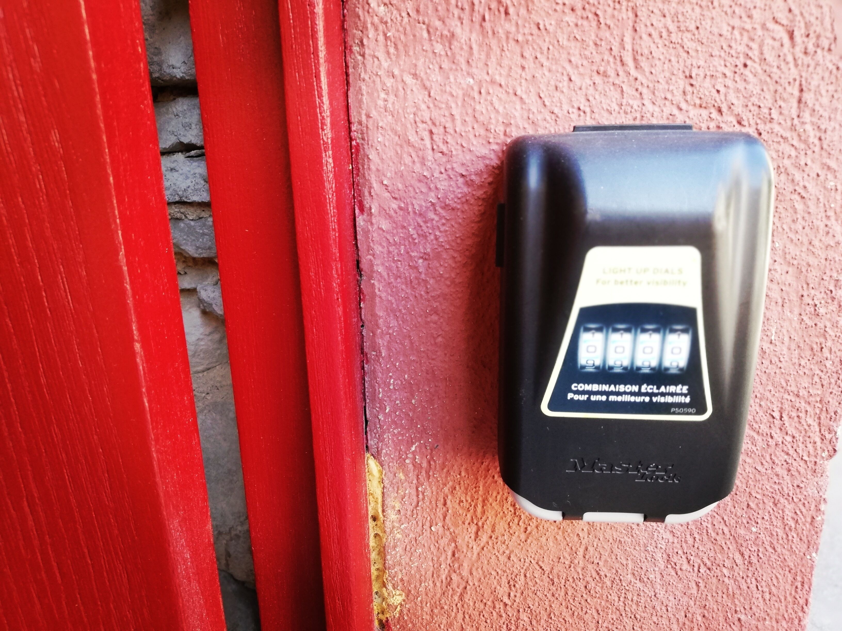 Un dispositivo de intercomunicador negro montado en una pared rosa con textura, junto a una puerta roja.