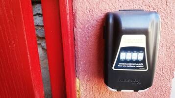 Un dispositivo de intercomunicador negro montado en una pared rosa con textura, junto a una puerta roja.