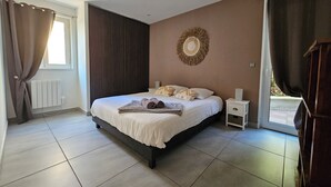 A bedroom with a large bed, a bedside table, a wall-mounted decorative item, and a view through a window.
