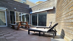 An outdoor patio with wooden furniture, including a table and two lounge chairs.
