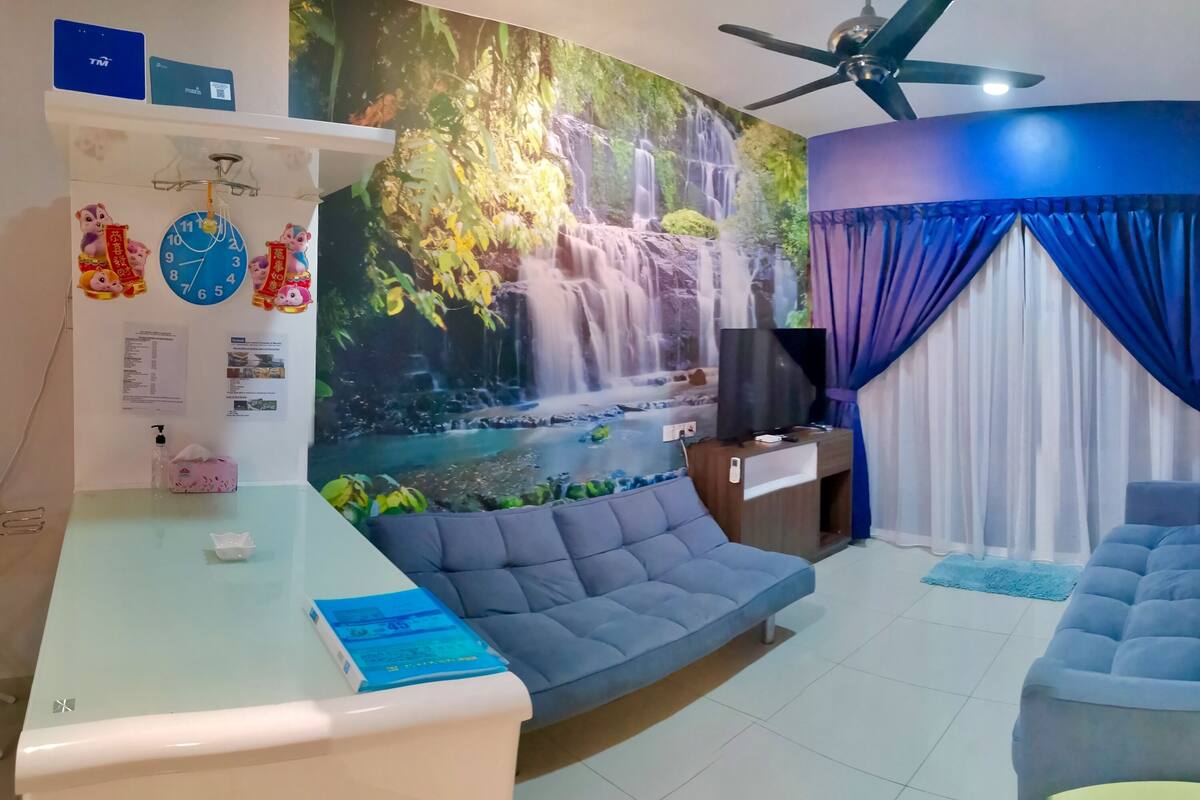 Ein Zimmer mit einer großen Wandmalerei eines Wasserfalls, einem Deckenventilator, einem Sofa, einem Fernseher und einem Schreibtisch mit einem Computer und einer Taschentuchbox.