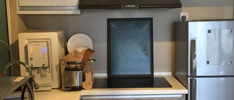 Una cocina moderna con armarios blancos, un refrigerador de acero inoxidable, una cafetera y una pizarra con la palabra 'LOVE'.