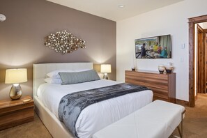 Une chambre avec un grand lit, deux tables de chevet avec des lampes, une tête de lit en bois, une œuvre d’art murale et un tableau encadré accroché au mur.