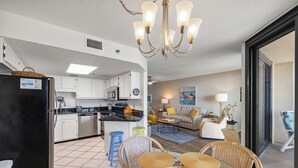 Une cuisine moderne avec des meubles blancs, un réfrigérateur noir et un coin repas comprenant des chaises en osier et une table en verre.