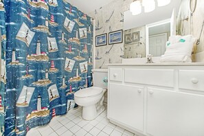 Ein Badezimmer mit einer Duschvorhangs mit Marine-Motiven, einer weißen Toilette und einem weißen Waschtisch mit Spiegel.