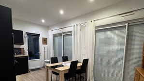A spacious room with a dining table, chairs, a kitchen area, and large sliding doors.